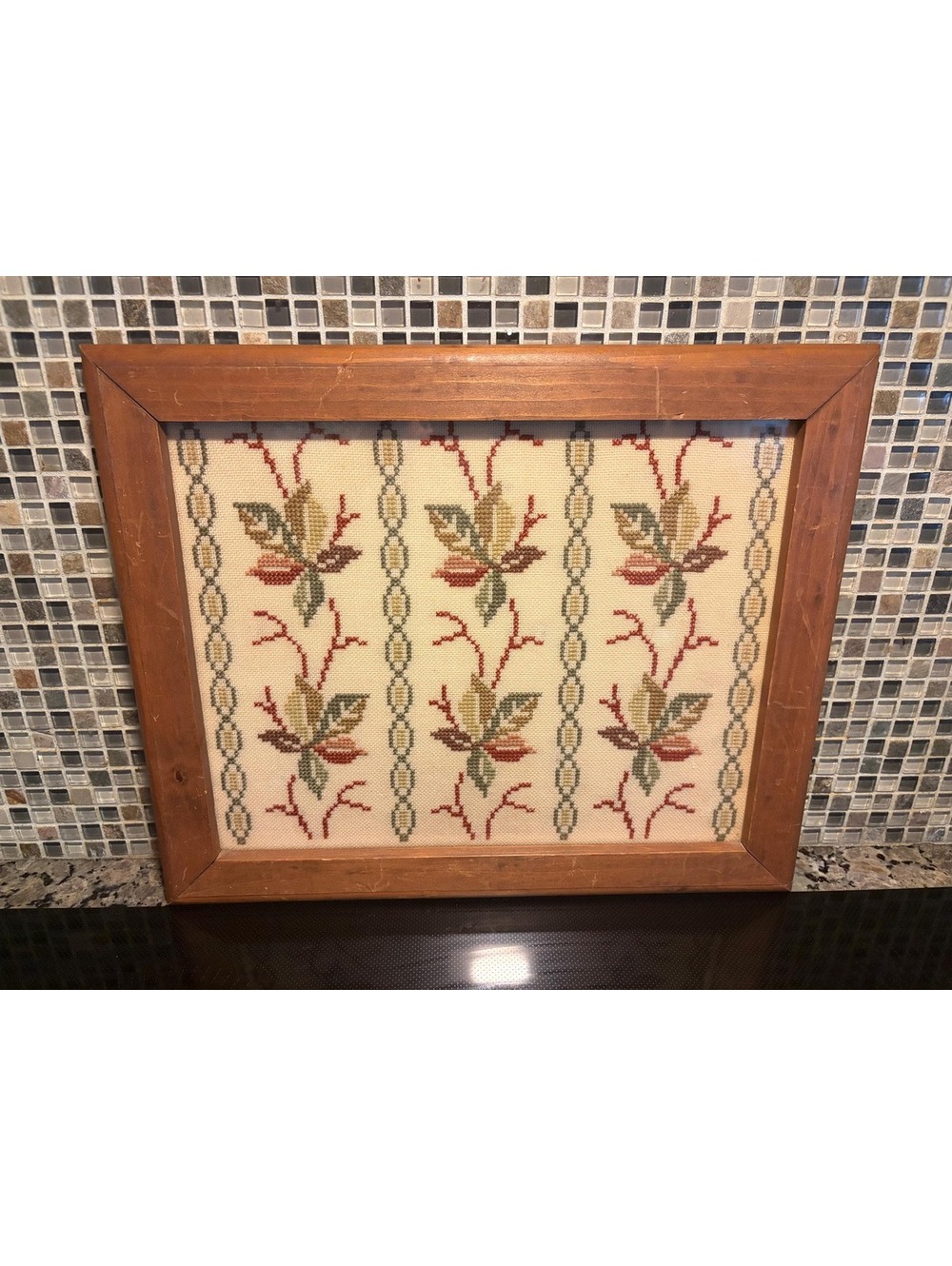 This is a vintage framed botanical cross-stitch or needlepoint textile panel.